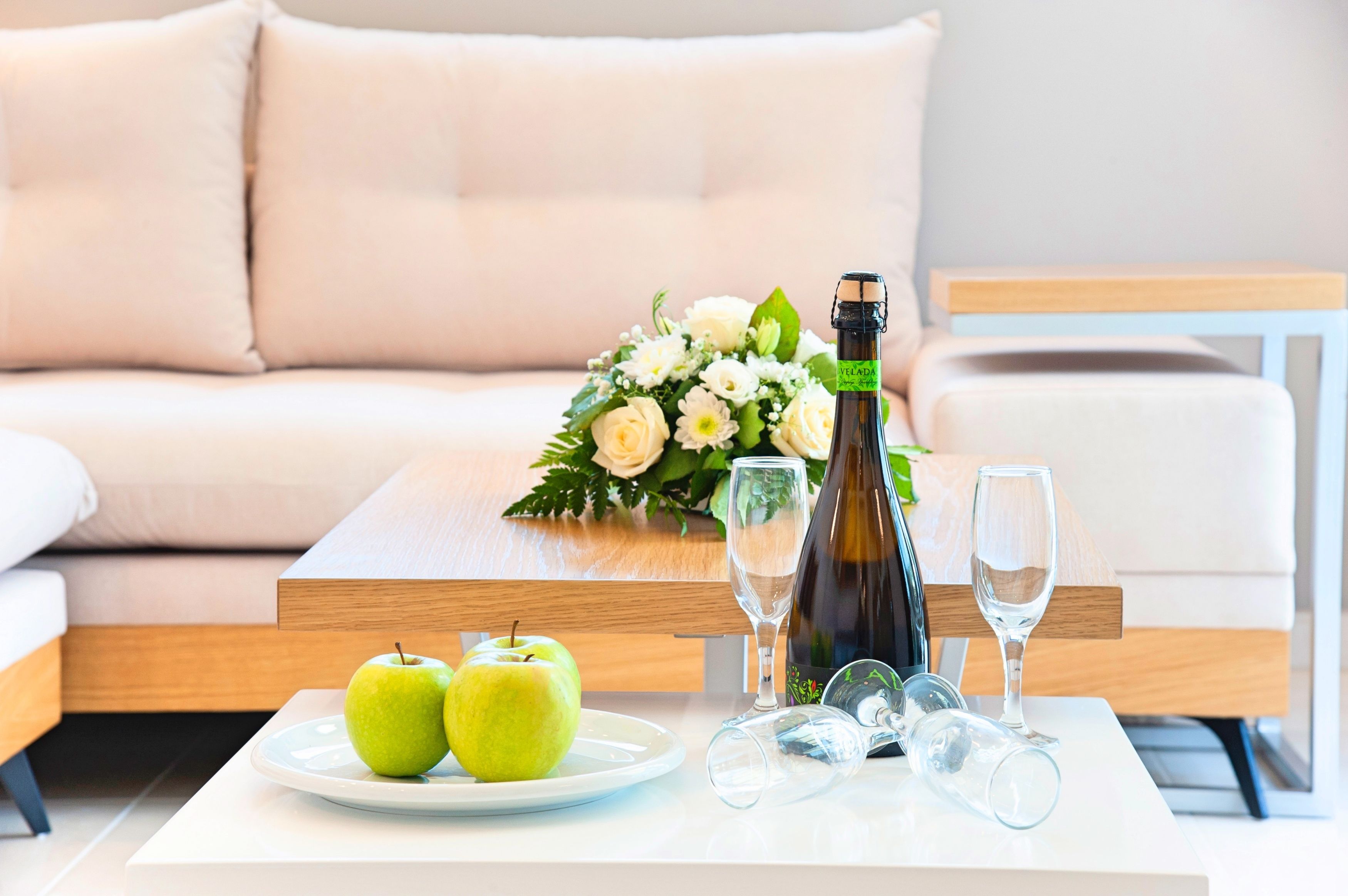 Un salon moderne avec un canapé, une table basse sur laquelle se trouvent une bouteille, des verres et deux pommes.