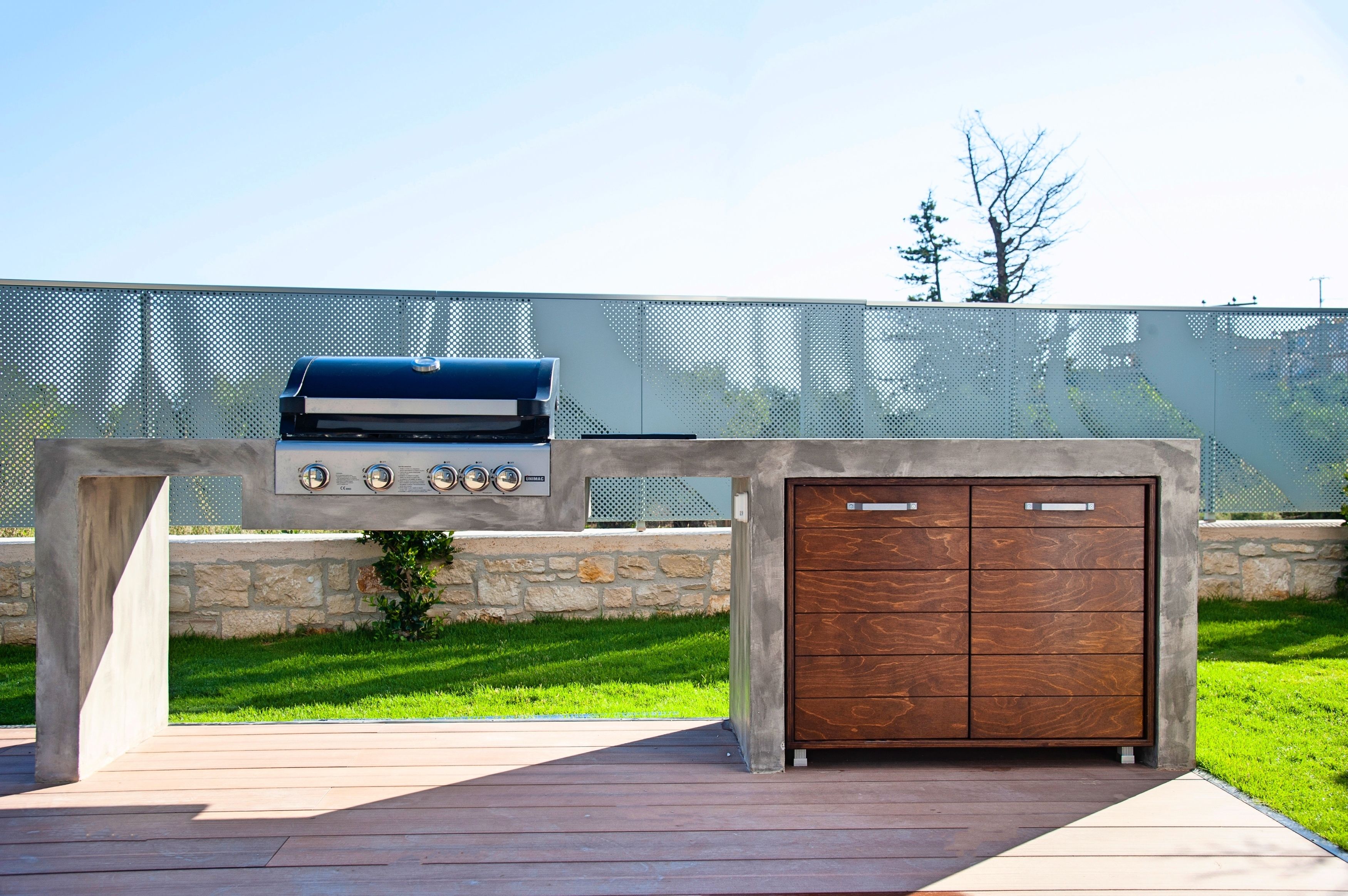 An outdoor kitchen with a grill, a built-in oven, and a wooden cabinet.