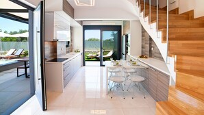 A modern kitchen with a dining area, a staircase, and a view of the outdoors. - Perla Villas with Heated Pool (Apokoronas)