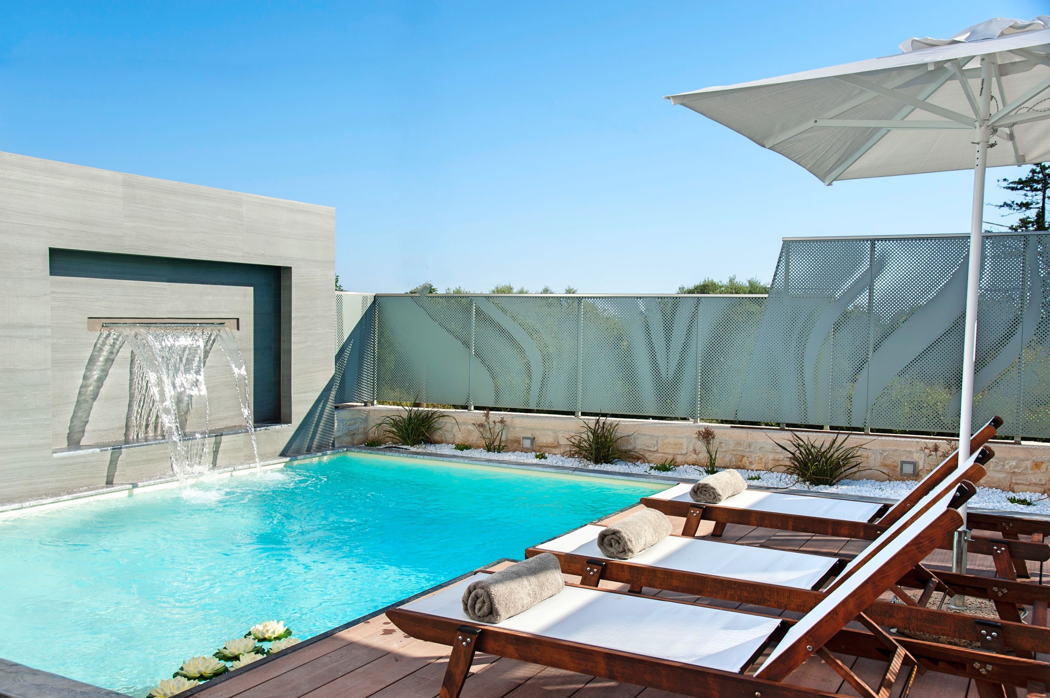 A modern outdoor pool area with lounge chairs and a waterfall feature.