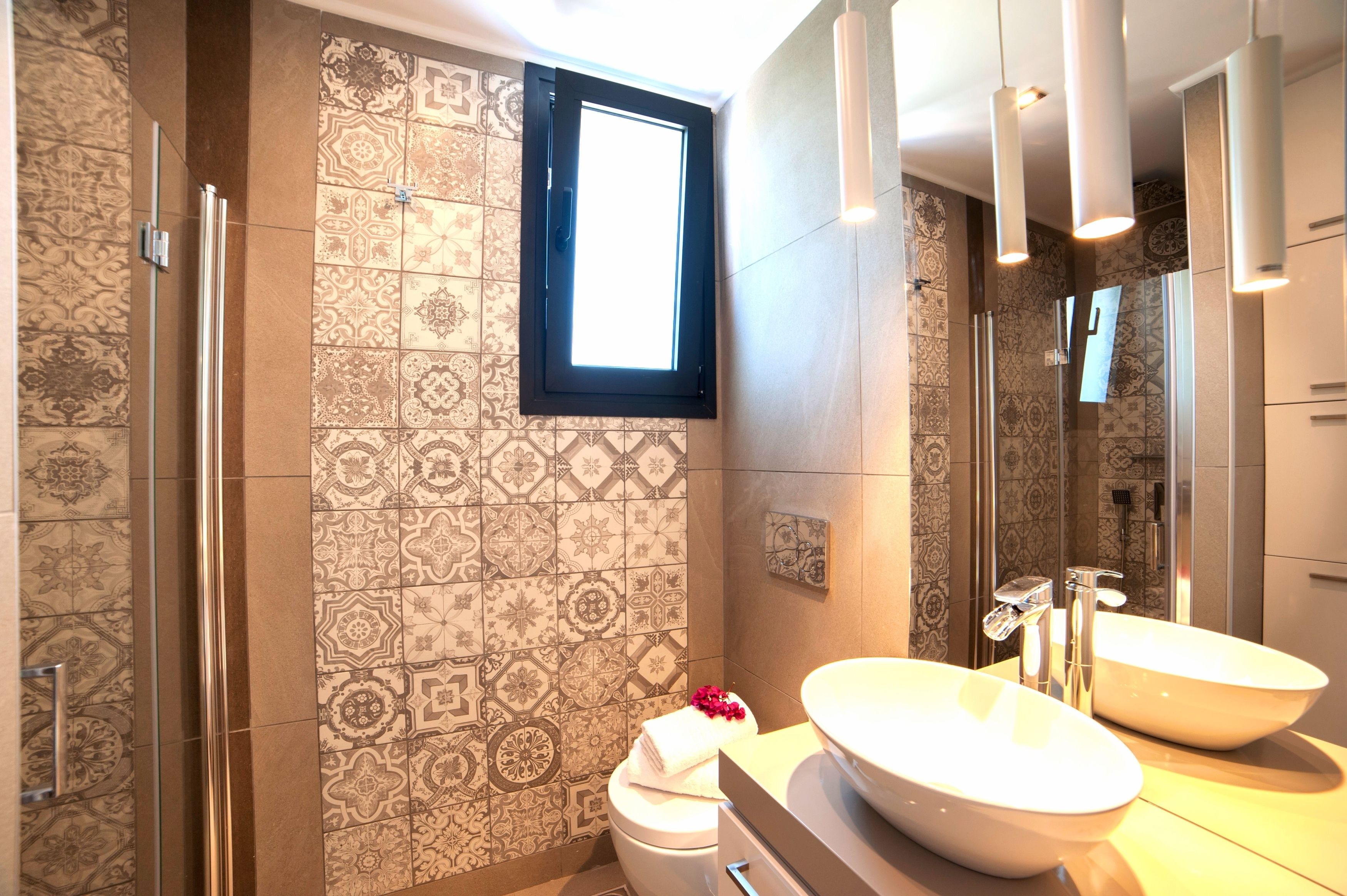 Un baño con azulejos estampados, un ventanal amplio, un lavamanos doble y una zona de ducha.
