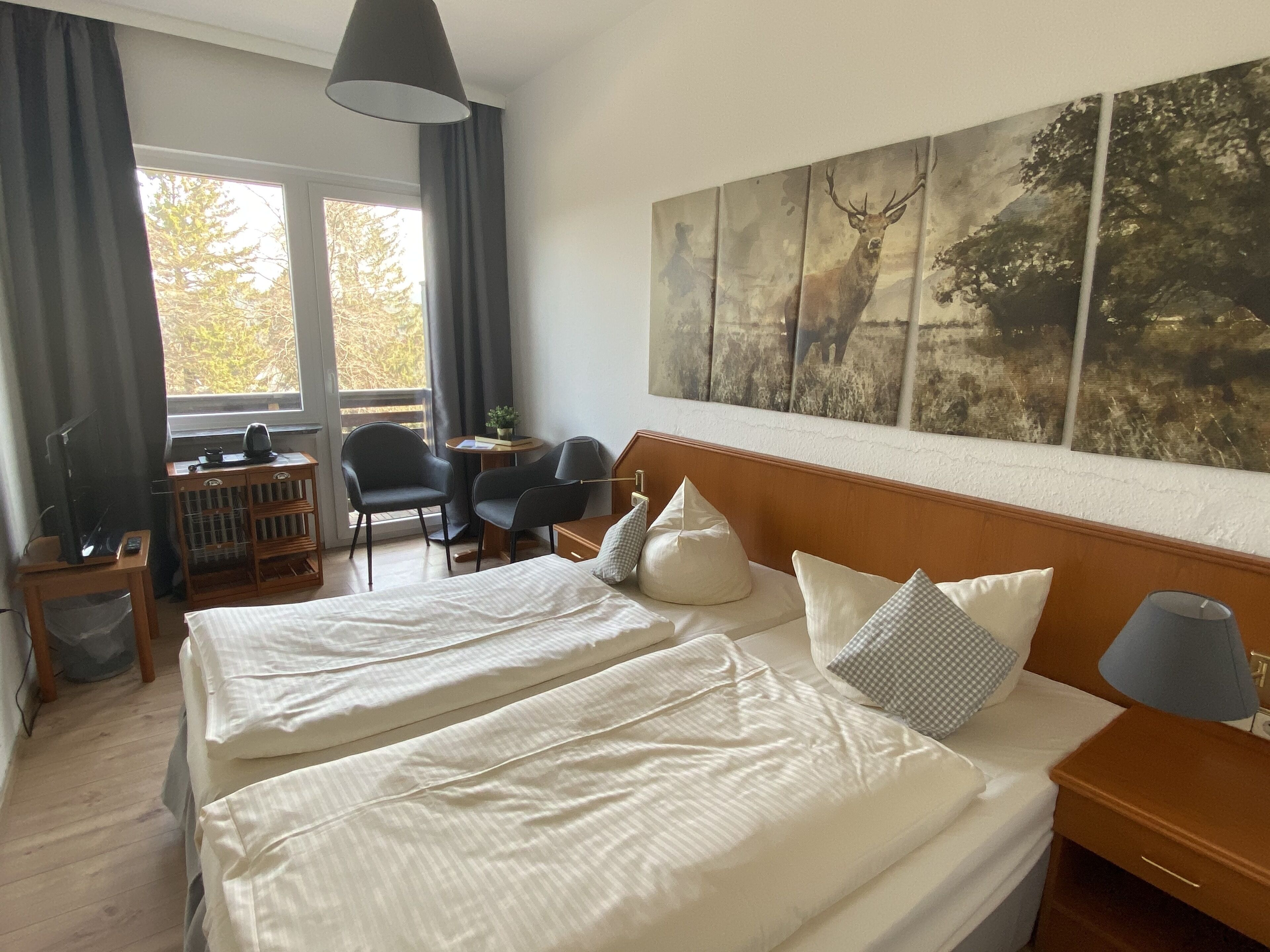 Een hotelkamer met twee bedden, een groot raam, een bureau met stoel, en een schilderij aan de muur.