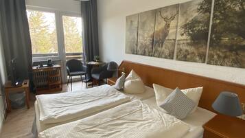 Een hotelkamer met twee bedden, een groot raam, een bureau met stoel, en een schilderij aan de muur.