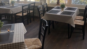 Uma sala de jantar com toalhas de mesa xadrez, cadeiras de madeira escura e vista para uma paisagem nevada através de grandes janelas.