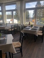 Uma sala de jantar com toalhas de mesa xadrez, cadeiras de madeira escura e vista para uma paisagem nevada através de grandes janelas.