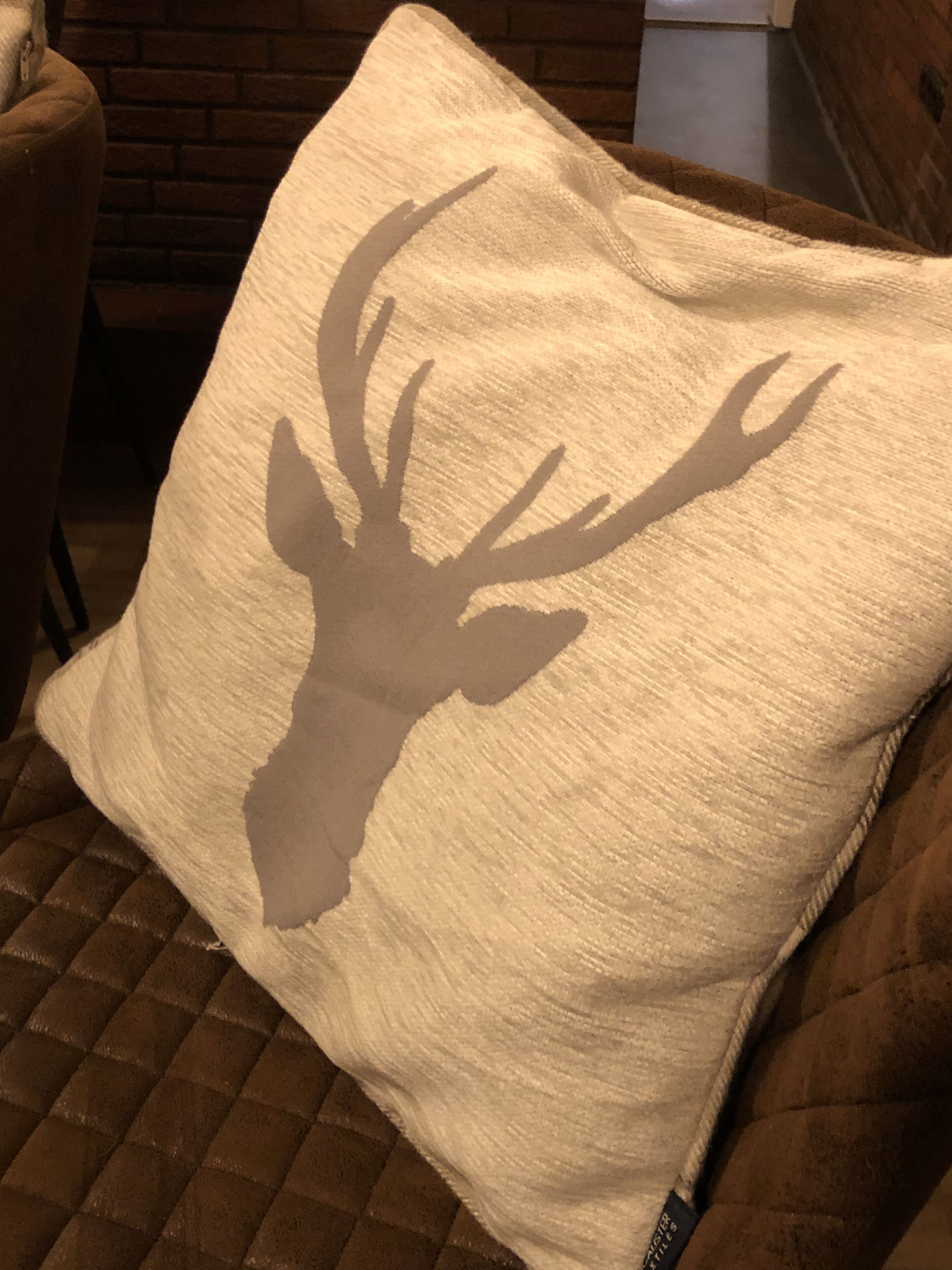 A pillow with a deer head silhouette on a brown couch.
