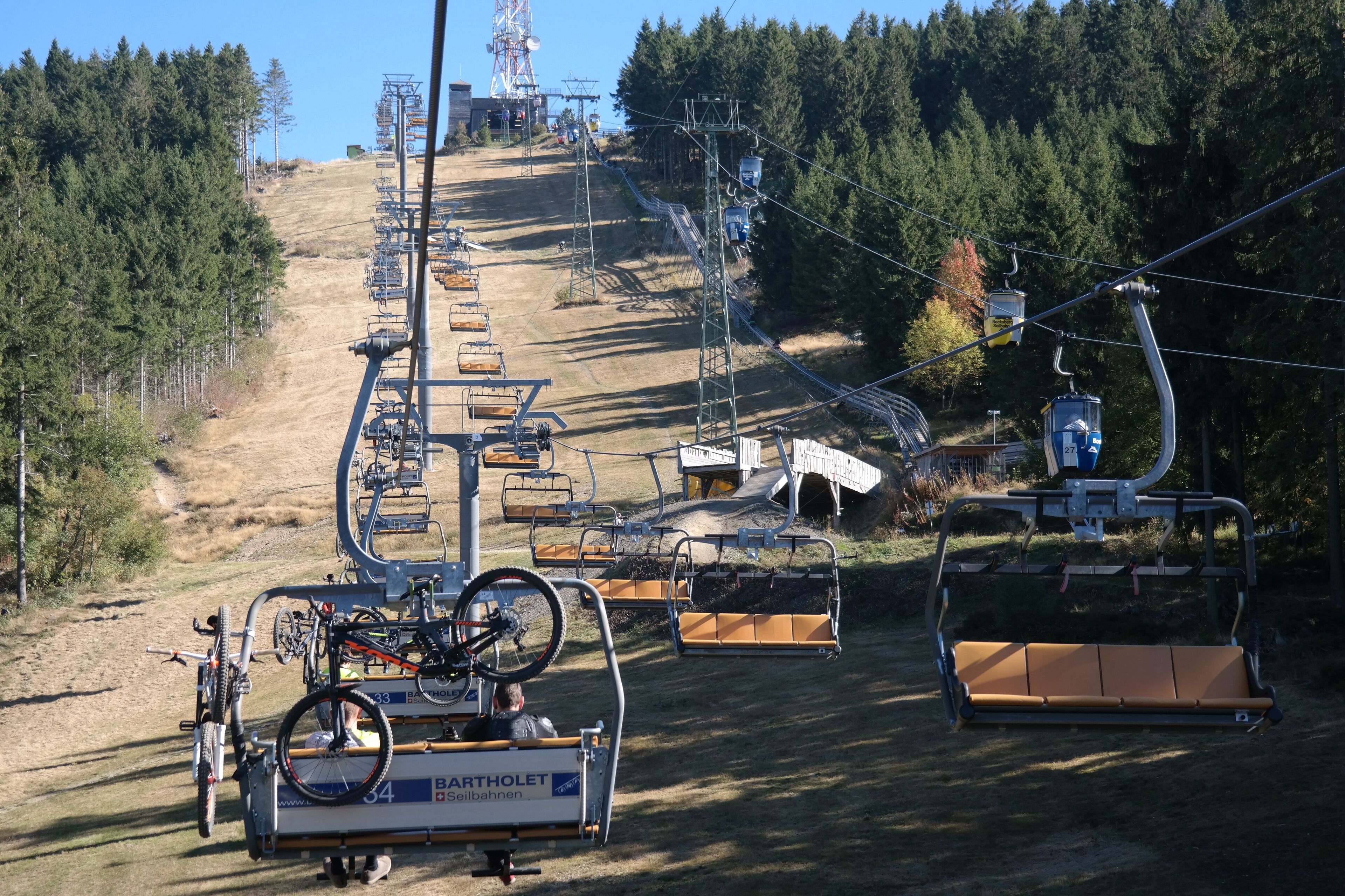 A ski lift with chairs and a cable system, surrounded by trees and a clear sky.