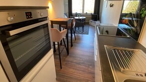 Uma cozinha compacta com forno embutido, exaustor de aço inoxidável e área de jantar com mesa e cadeiras.