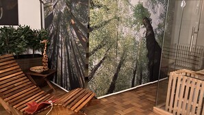 Quarto com um grande mural com tema de floresta, um banco de madeira, uma pequena mesa com um objeto decorativo e um painel de vidro.