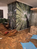 Quarto com um grande mural com tema de floresta, um banco de madeira, uma pequena mesa com um objeto decorativo e um painel de vidro.