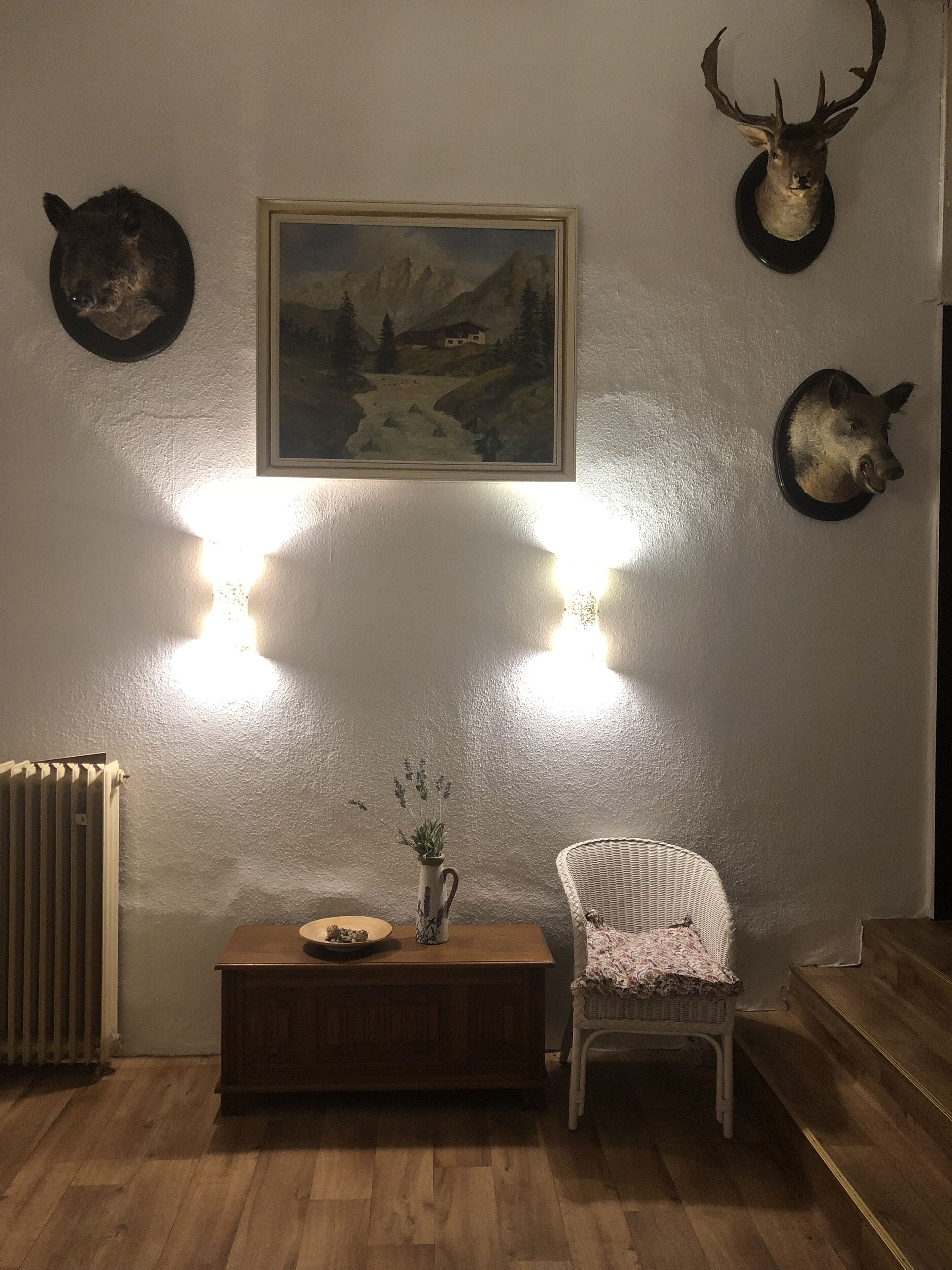 A room with a wooden cabinet, a white wicker chair, and two mounted animal heads.