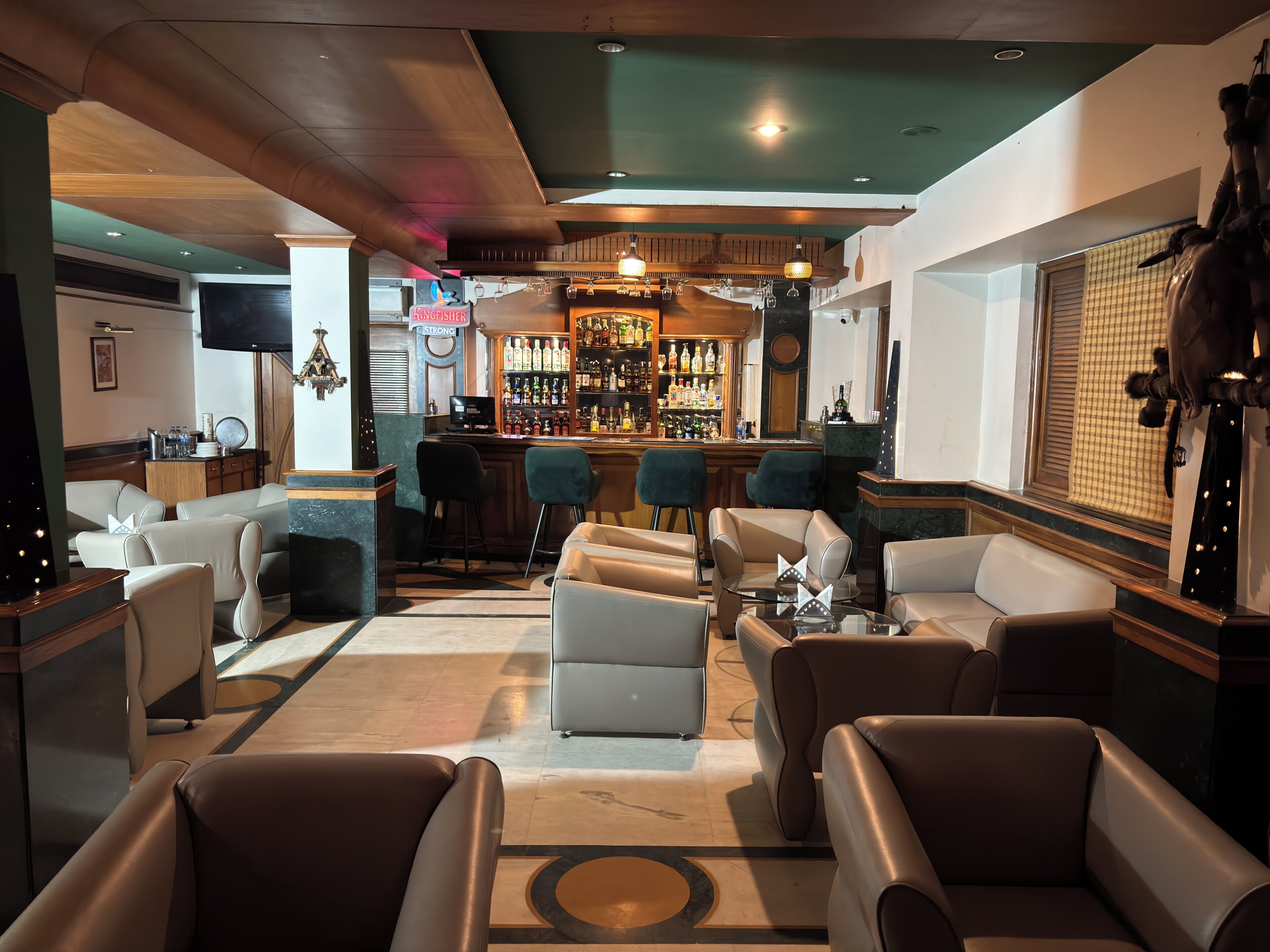 Uma área de bar com mostruário de bebidas, assentos de couro e uma televisão.