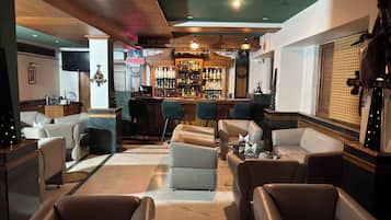 Uma área de bar com mostruário de bebidas, assentos de couro e uma televisão.