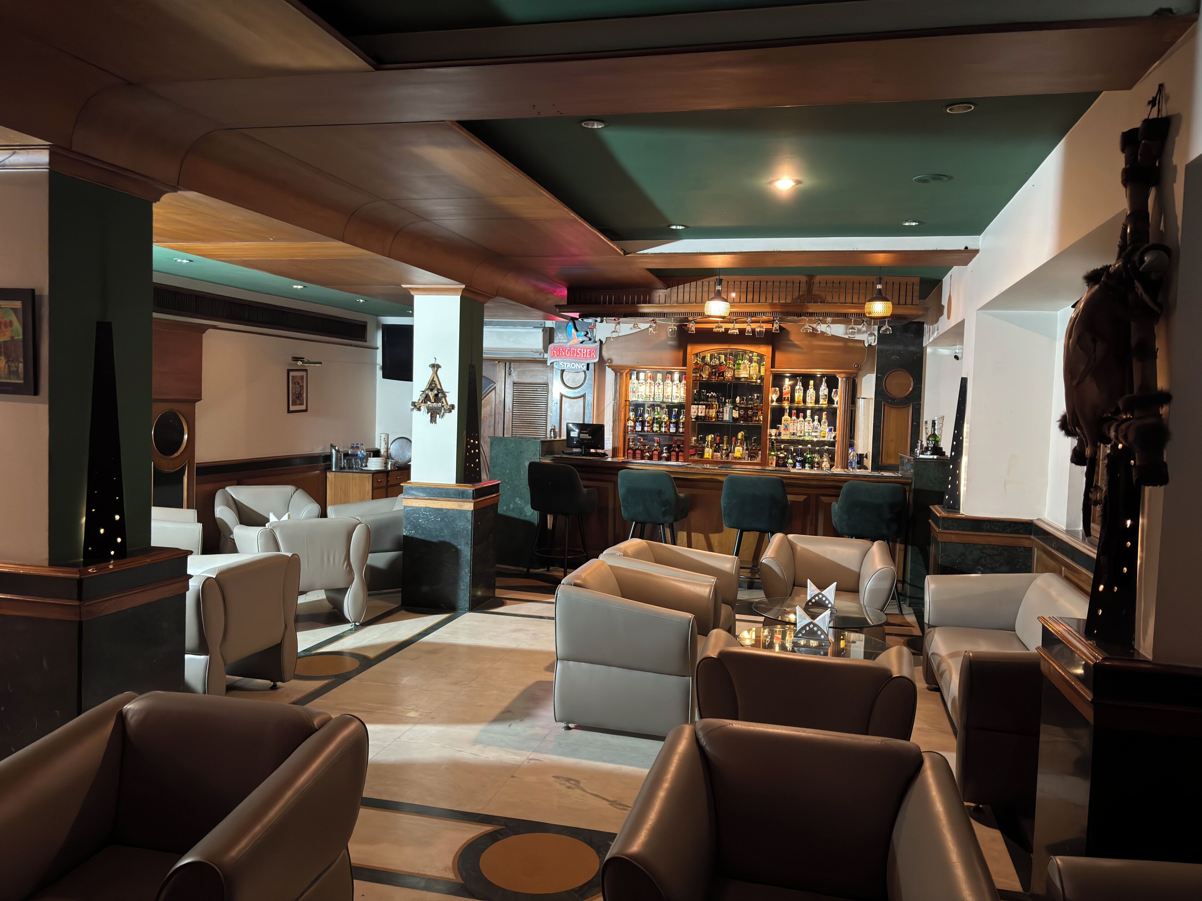 Eine Bar mit einer Holztresen, verschiedenen Sitzgelegenheiten, darunter Barhocker und gepolsterte Stühle, sowie einer Auswahl an Spirituosenflaschen auf Regalen.