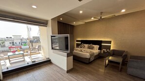 Una habitación de hotel moderna con una cama grande, televisión, sofá y balcón con vista a la ciudad.