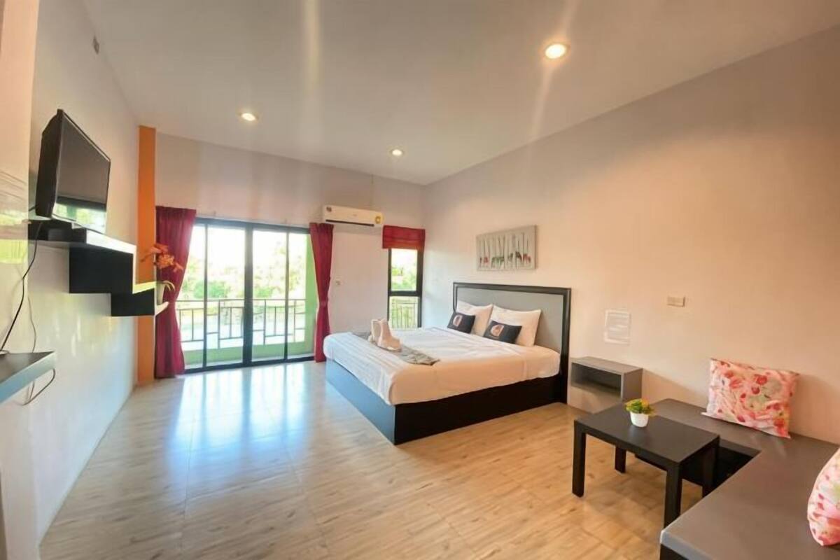 A modern hotel room with a large bed, a TV, a small table, and a balcony.