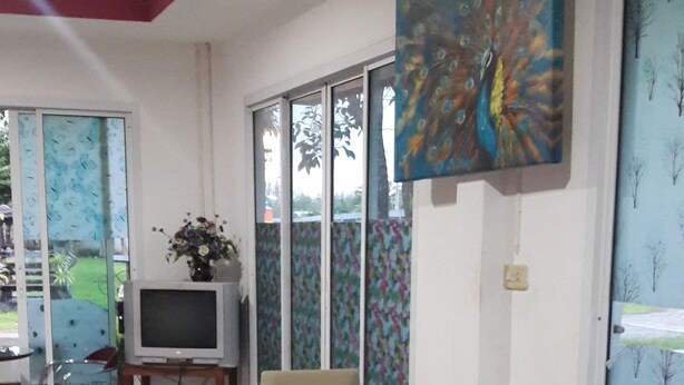 A dining area with a glass table, four chairs, a television on a stand, and a colorful painting on the wall. - RoomQuest Chonburi Phanat Nikhom (Phanat Nikhom)