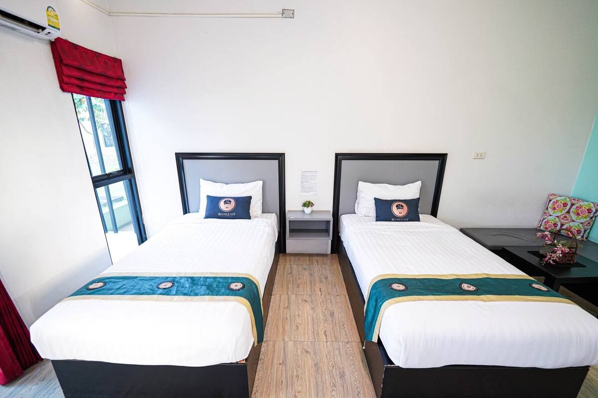 A double room with two beds, each with a headboard, a small bedside table, and a window with red curtains.