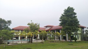 A building with a red roof and multiple windows, surrounded by green grass and trees. - RoomQuest Chonburi Phanat Nikhom (Phanat Nikhom)