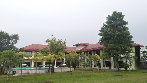 A building with a red roof and multiple windows, surrounded by green grass and trees. - RoomQuest Chonburi Phanat Nikhom (Phanat Nikhom)