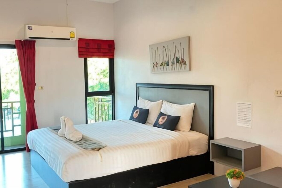 A bedroom with a bed, a bedside table, a window, and a wall-mounted air conditioner.