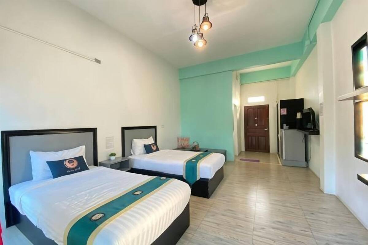 A hotel room with two beds, a TV, a refrigerator, and a bathroom visible through an open door.