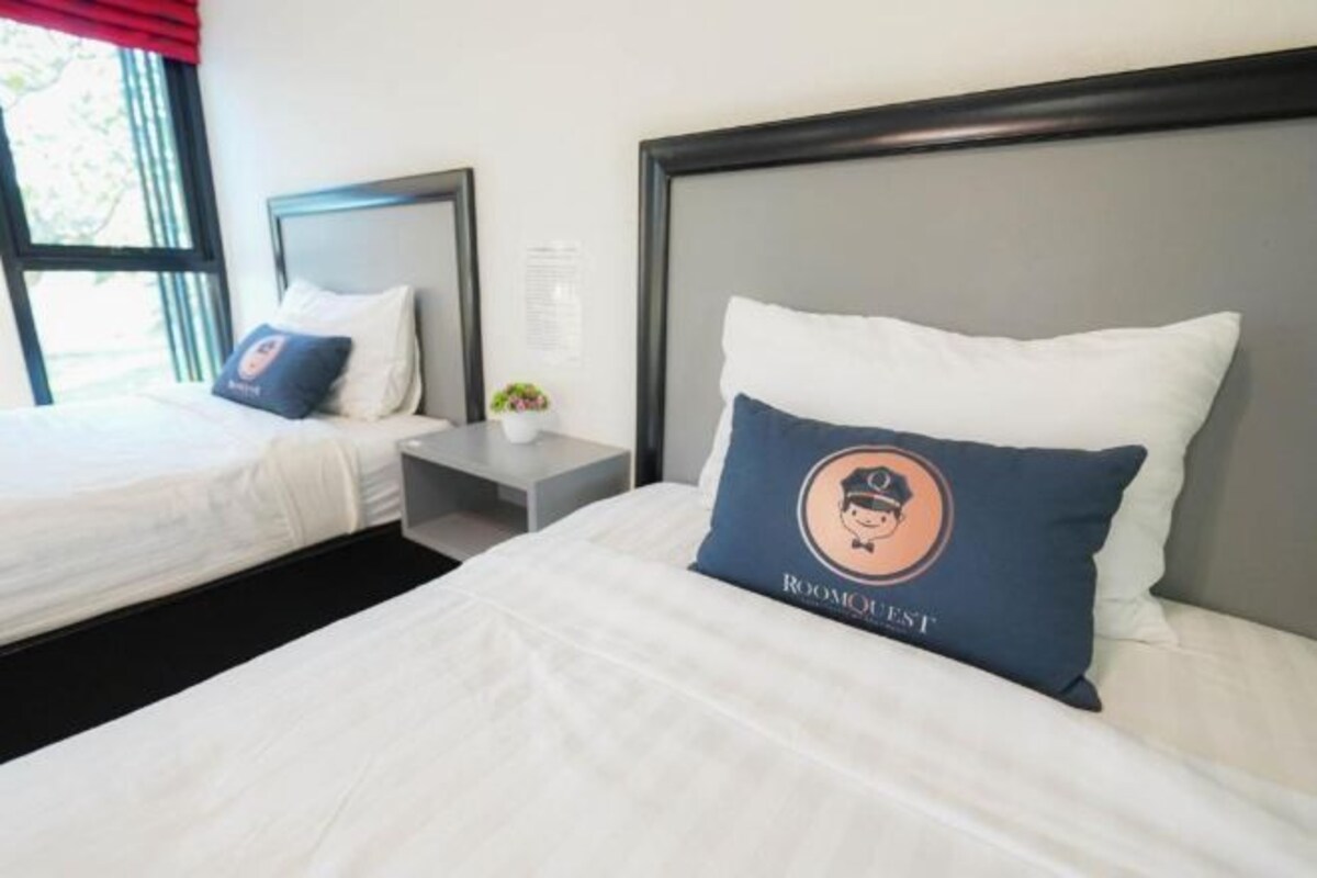A hotel room with two beds, a nightstand, and a window with curtains.