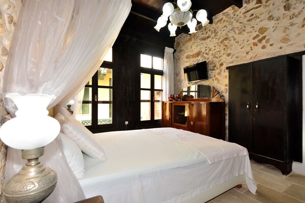 A bedroom with a bed, a wooden wardrobe, a television on the wall, and a chandelier. - Antonia's House (Rethymno)