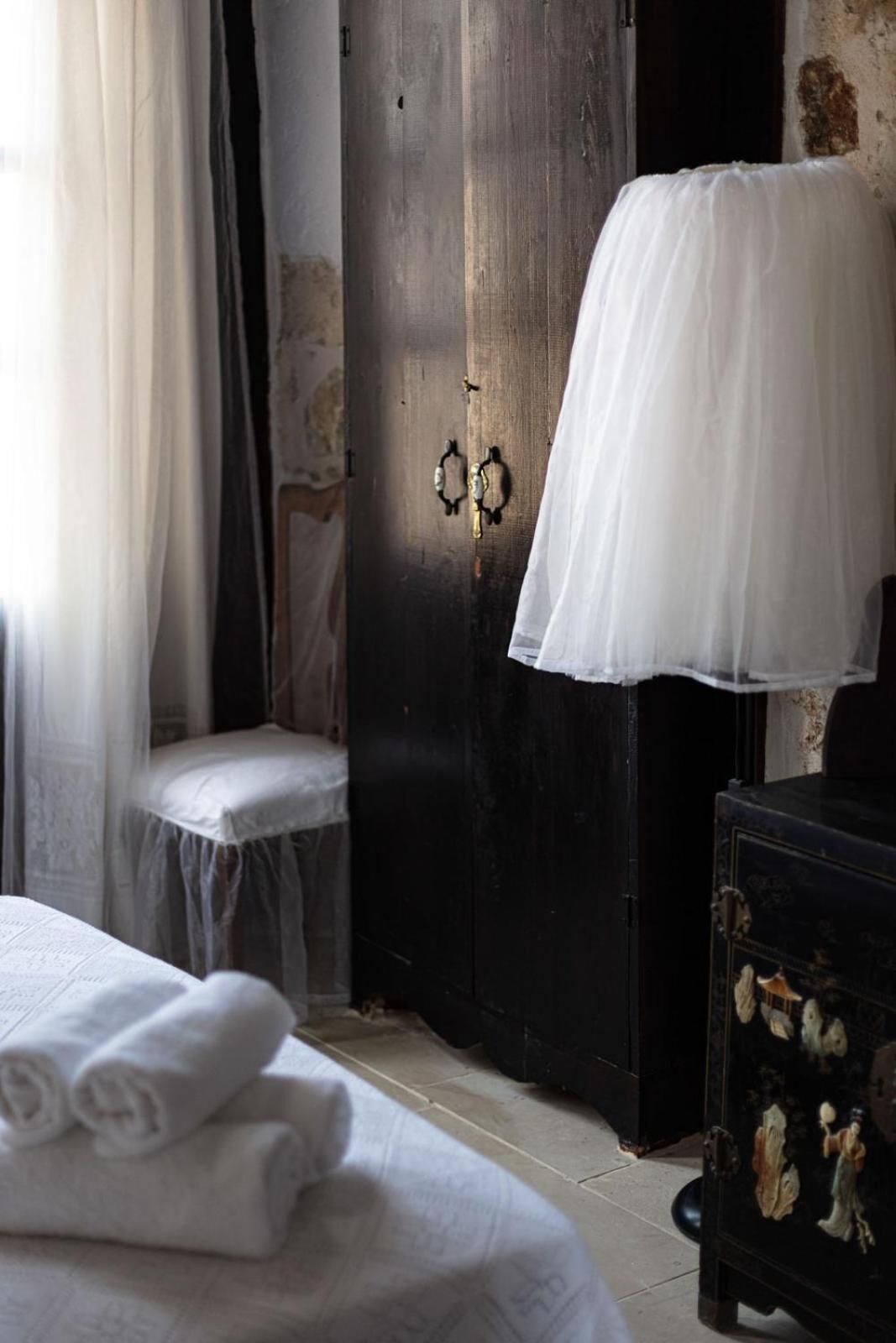Um quarto com cama, um banco, uma porta de madeira e um abajur.