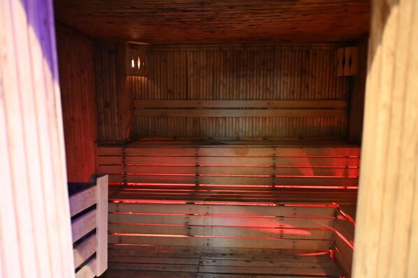 A sauna with wooden walls and benches, featuring red heating elements. - Barden Hotel (Siirt)