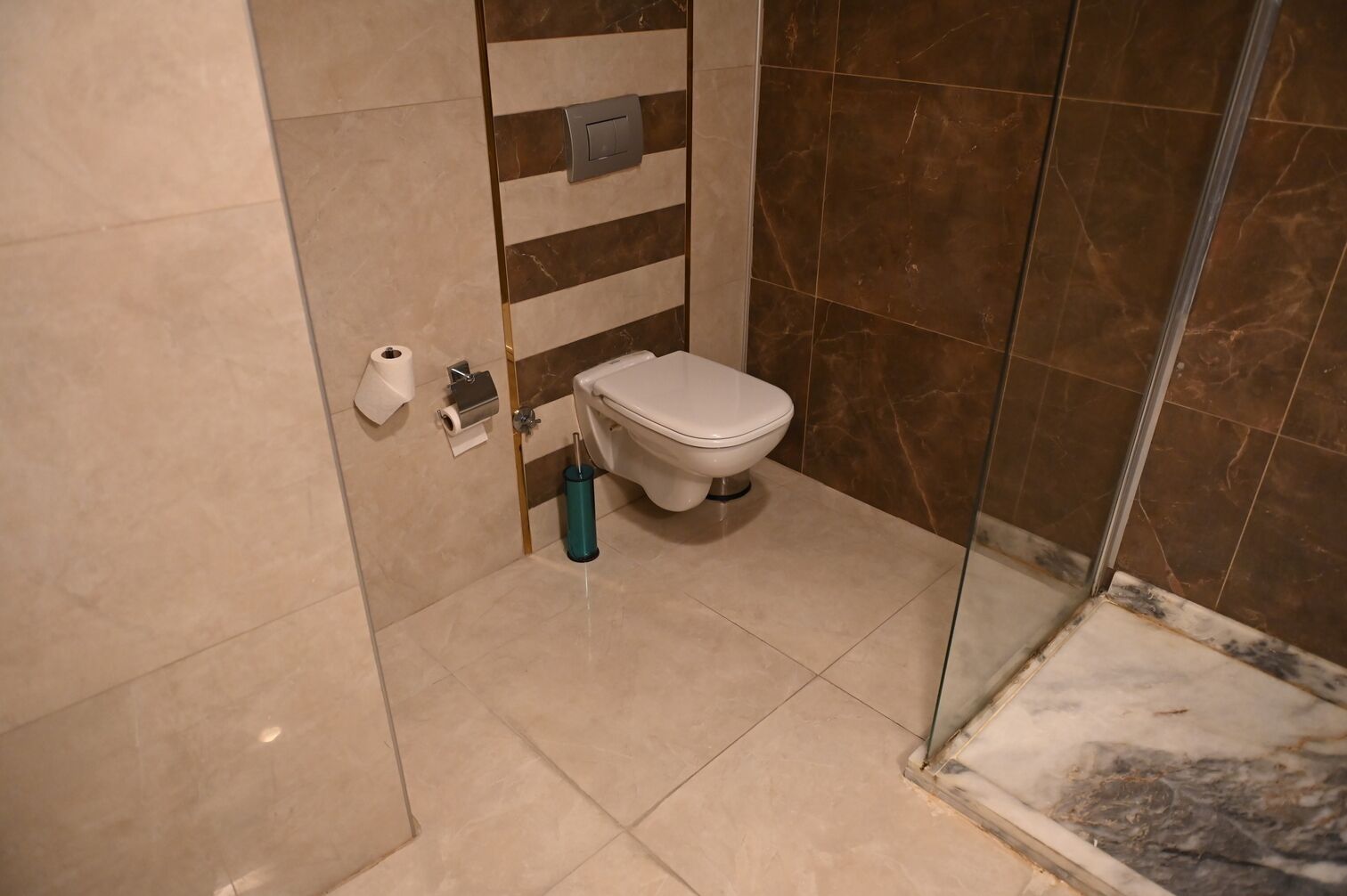 A bathroom with a toilet, a trash bin, and a shower area.