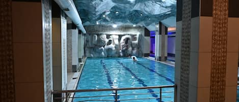 An indoor swimming pool with a rocky wall backdrop and a ceiling with a wave-like design.