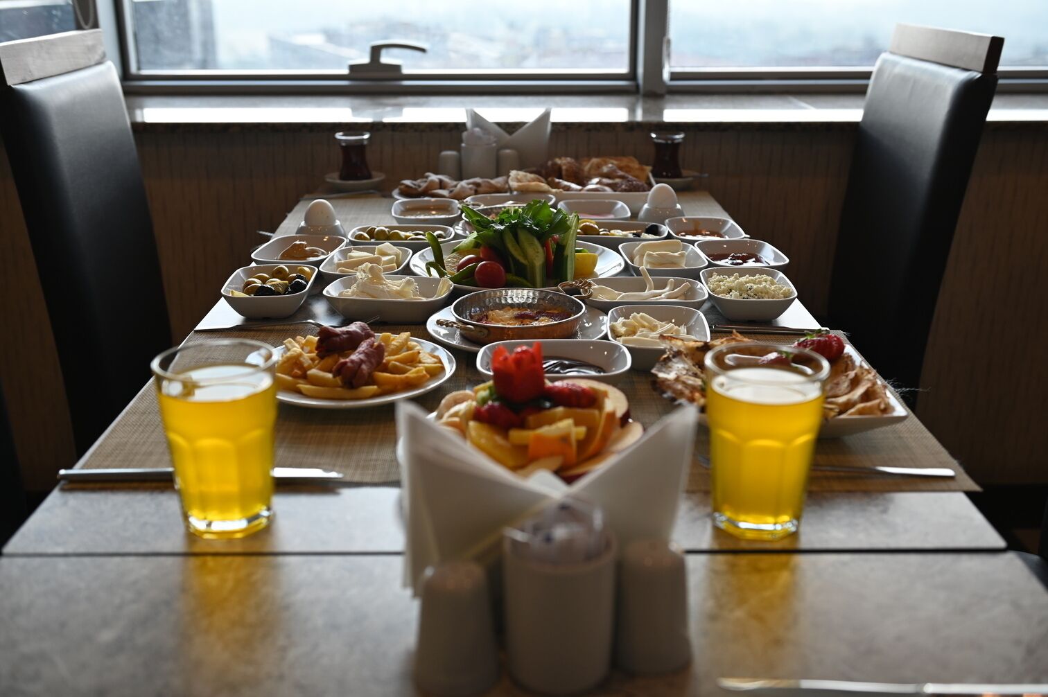 Una mesa de comedor con diversos platos y bebidas, ubicada en una habitación con vistas a través de una ventana.