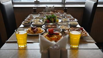 Una mesa de comedor con diversos platos y bebidas, ubicada en una habitación con vistas a través de una ventana.