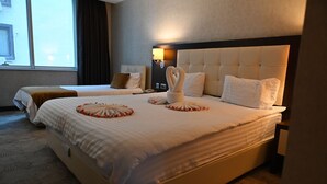 A hotel room with two beds, each with a headboard and pillows. There is a bedside table with a lamp and a phone. The room has a large window with curtains. - Barden Hotel (Siirt)