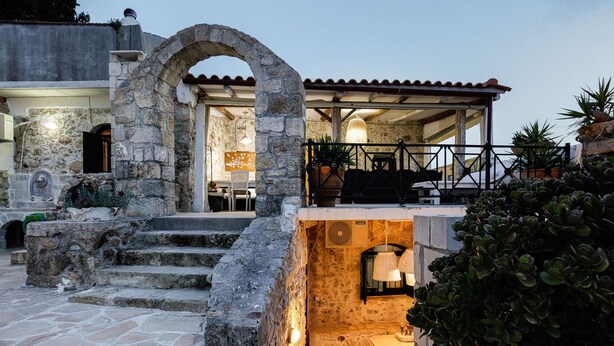 A stone archway leading to a covered outdoor area with a table and chairs, surrounded by potted plants and a stone staircase. - Villa Antonia (Rethymno)