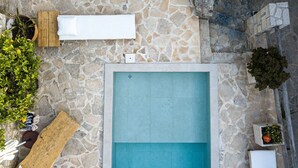 A stone pool with a wooden deck and lounge chairs. - Villa Antonia (Rethymno)