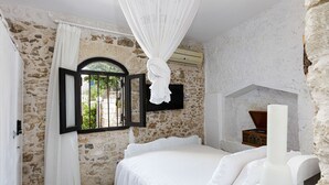 A bedroom with stone walls, a bed with white bedding, a window with black shutters, and a white canopy. - Villa Antonia (Rethymno)