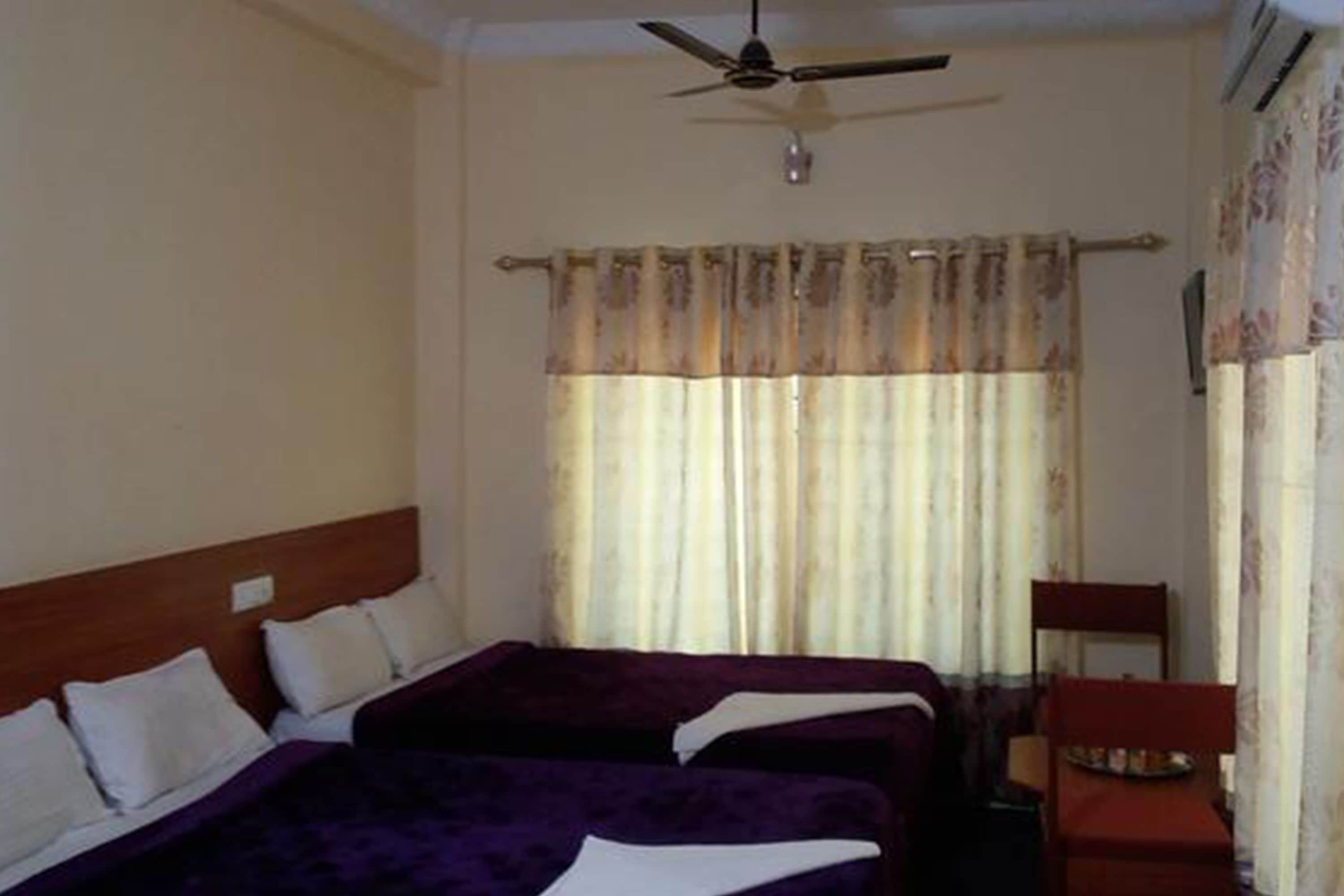 A hotel room with two beds, a ceiling fan, and a chair.