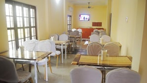 Un comedor con varias mesas y sillas, un televisor montado en la pared y un ventilador de techo.