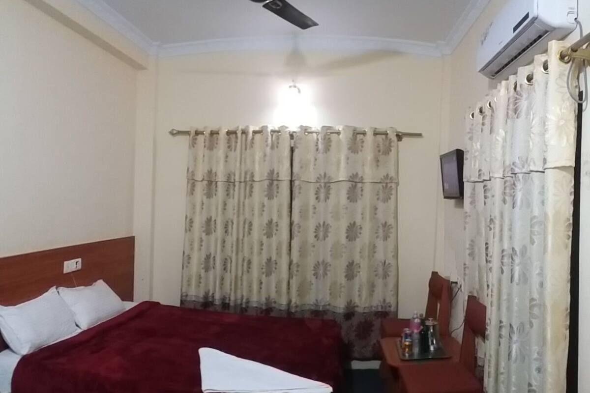 Quarto de hotel com uma cama, escrivaninha, cadeira, ventoinha no teto e ar condicionado.
