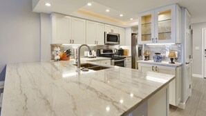 A modern kitchen with white cabinetry, a marble countertop, and stainless steel appliances.