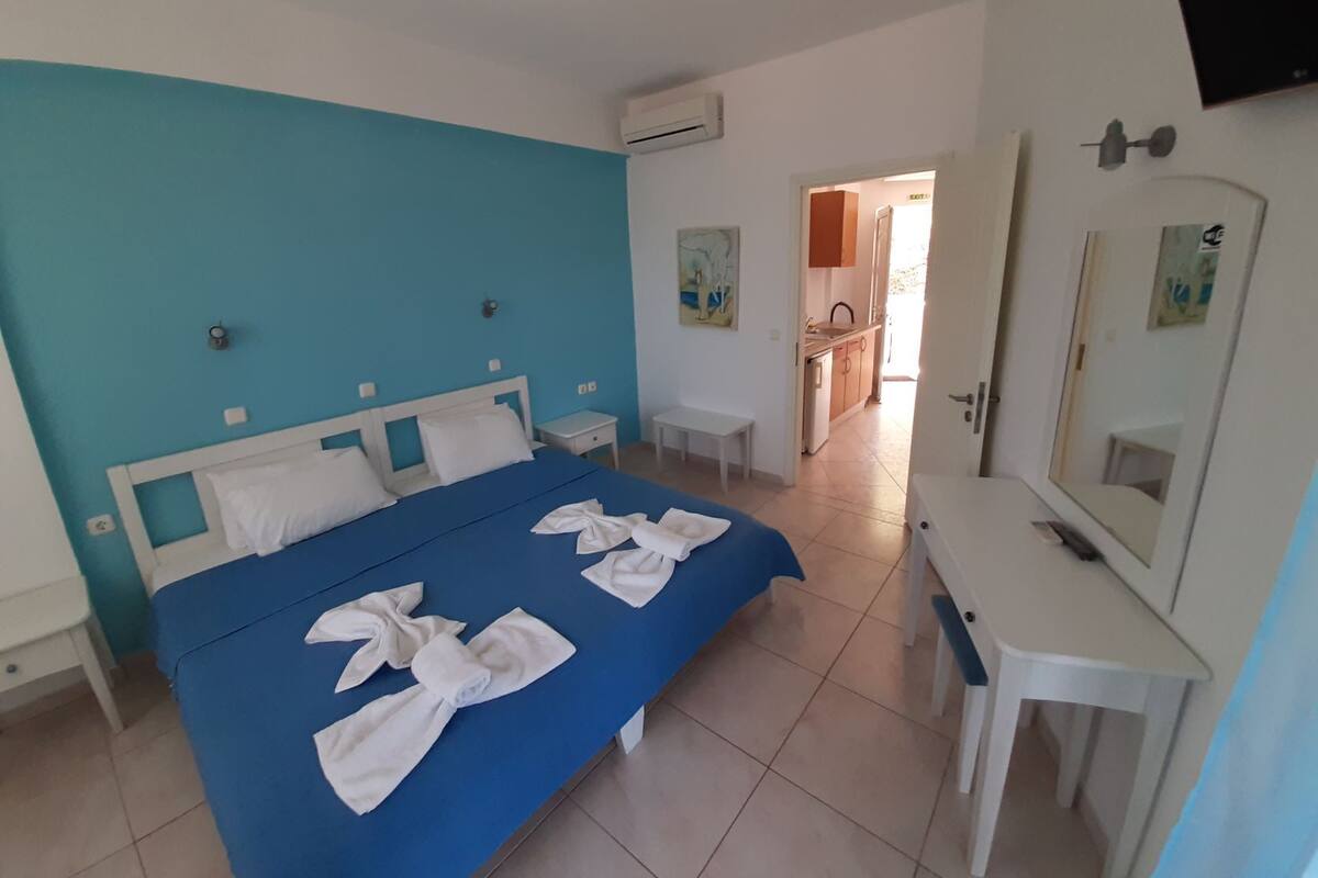 Ein Hotelzimmer mit Bett, Nachttisch, Spiegel und einem durch eine offene Tür einsehbaren Badezimmer.