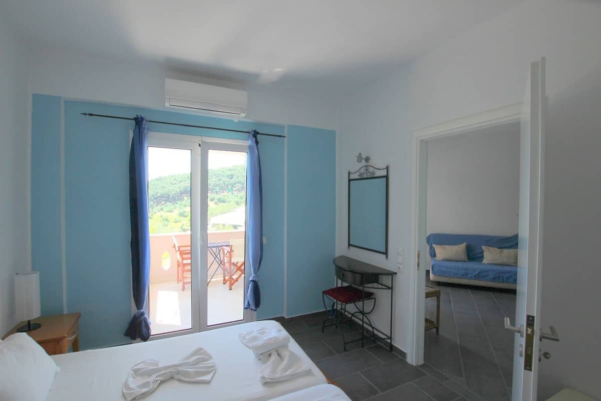 Ein Schlafzimmer mit Bett, Schreibtisch, Sessel, Balkon und einer Couch.