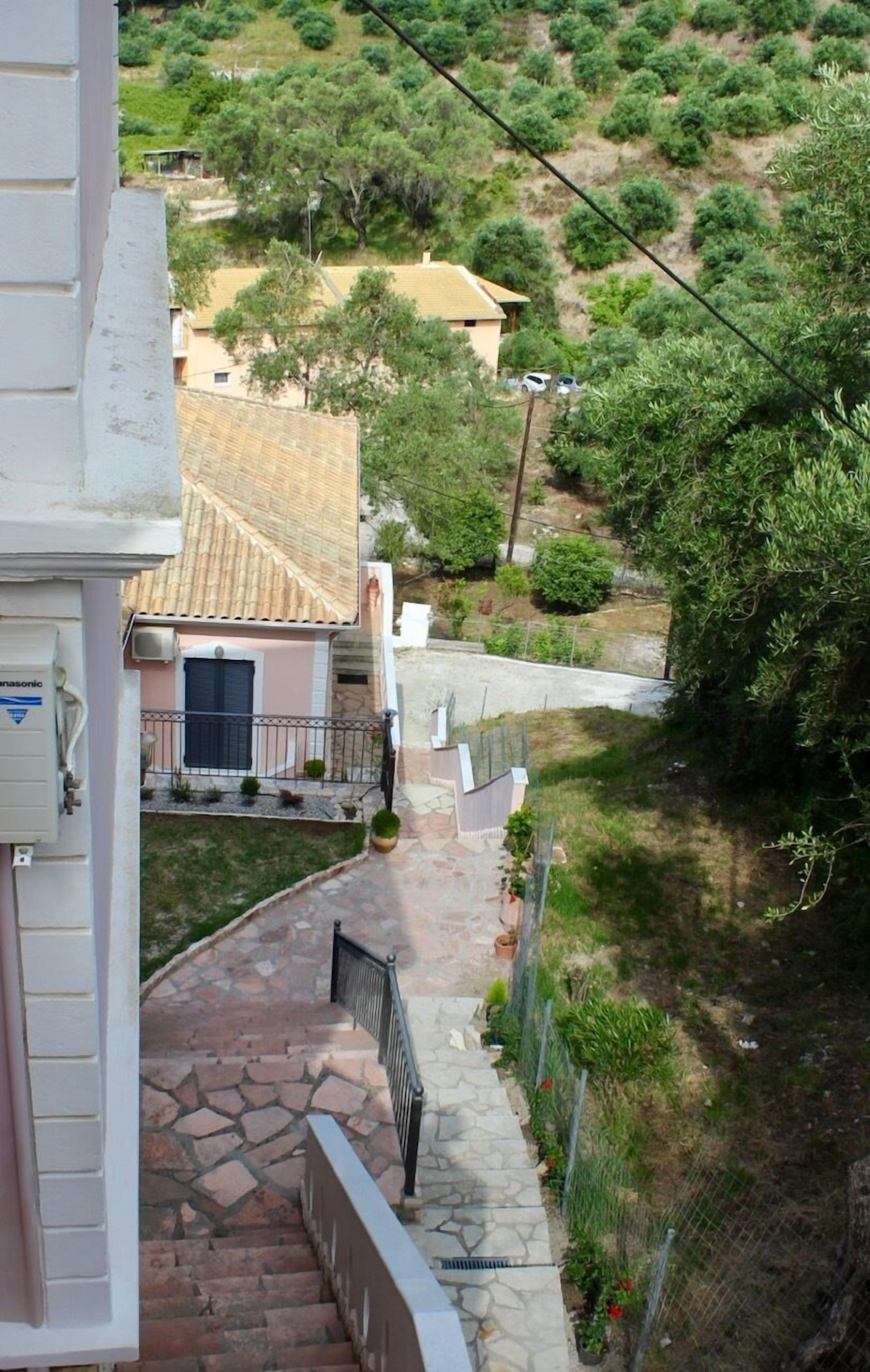 A stone staircase leading to a house with a tiled roof, surrounded by greenery and a fence.