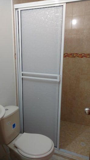 A bathroom with a toilet, a shower enclosure, and a tiled floor.