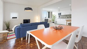 A modern living room with a blue sofa, a white dining table, and a kitchen in the background. - Elias Garcia II, apartment in the city center (Funchal)