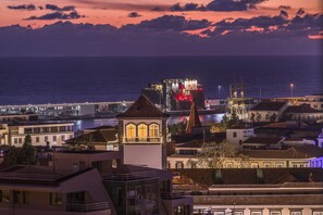 A coastal cityscape at dusk with a prominent building featuring a tower and a bridge in the foreground. - Elias Garcia II, apartment in the city center (Funchal)