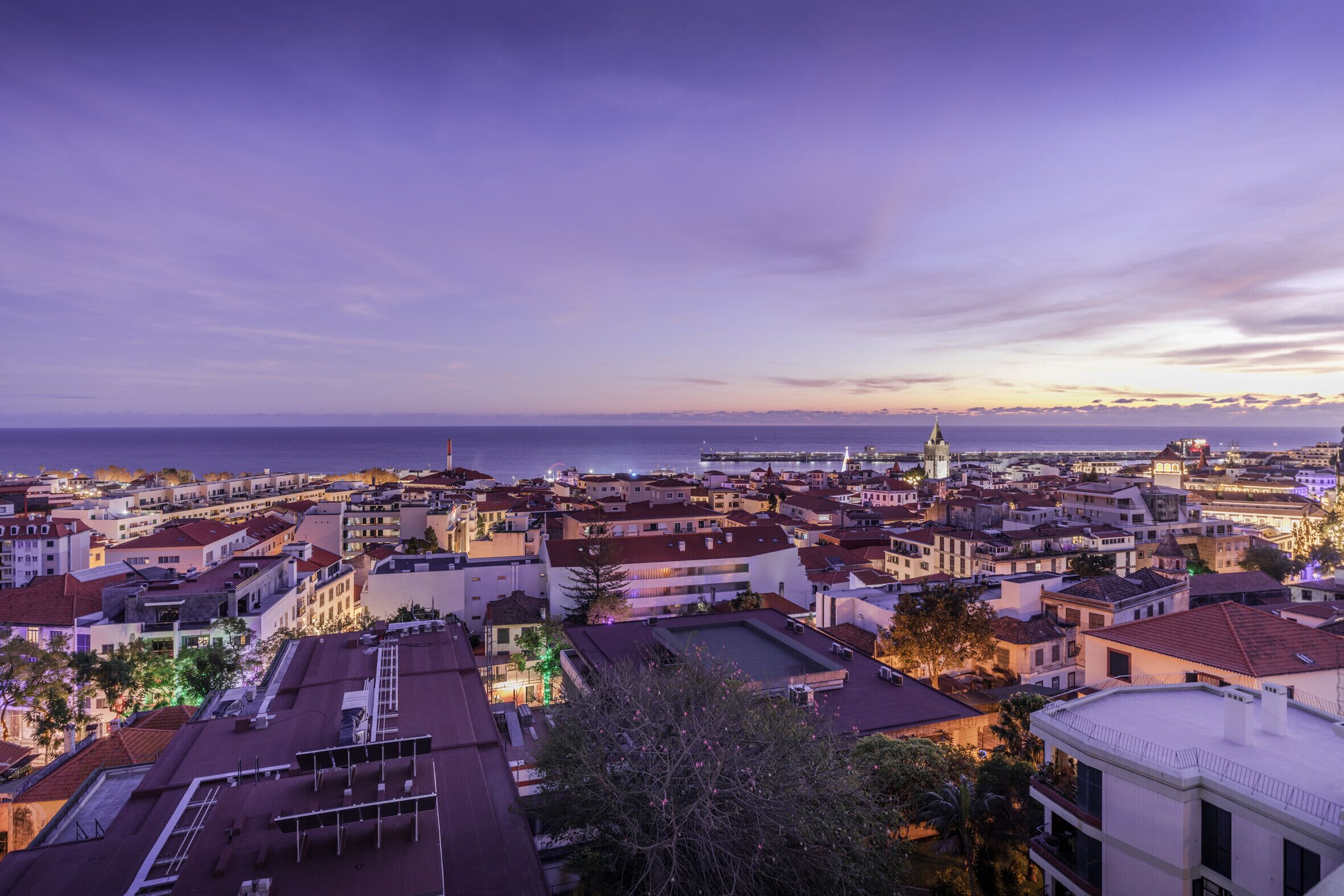 Une vue panoramique sur une ville au crépuscule, avec ses bâtiments et une église, prise depuis un point d’observation élevé.