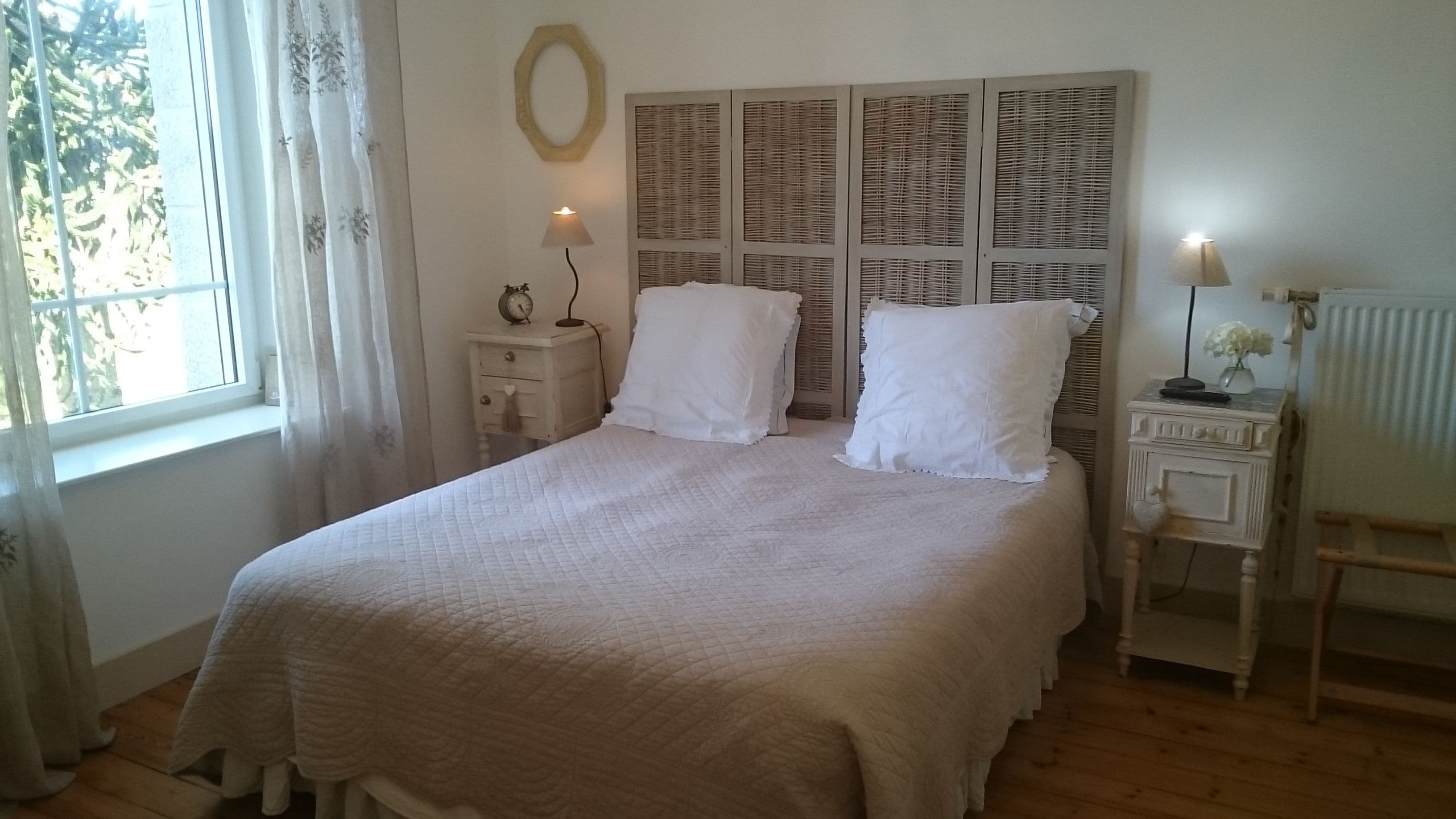 Un dormitorio con una cama grande, una mesita de noche con lámpara, un espejo y un radiador.